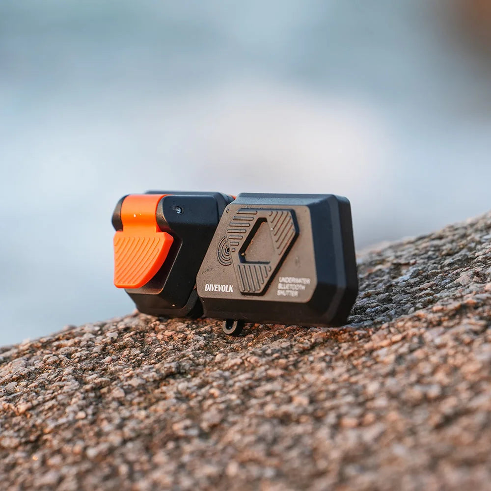 Divevolk external shutter with orange button displayed on coastal rocks
